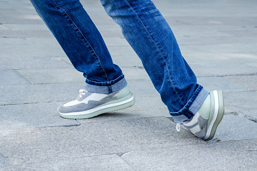 close-up of a woman's feet in jeans and sneakers tripping over unevenly laid paving slabs. Accident, injury on a walk due to poor road surface.