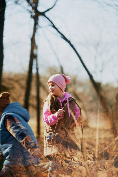 Little children, in warm jacket and cap finding joy in simple stick, surrounded by trees. Outdoor activities for children's development.