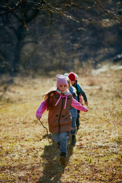istock Little girl in pink hat strides confidently ahead while boy, classmate follows on rustic trail. Outdoor activities for children's development. 2083861845