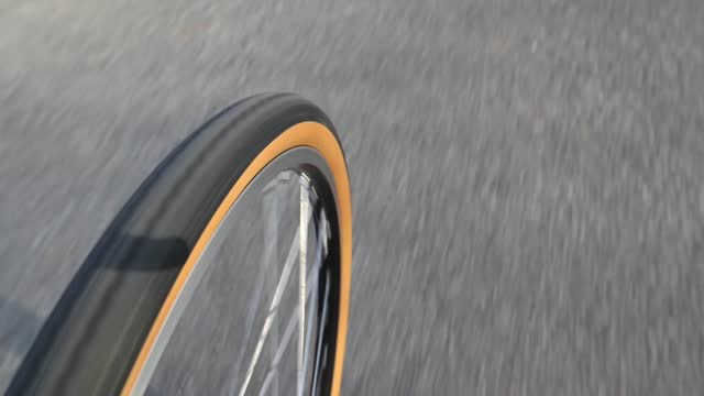 bike tire rolling on asphalt close up footage (bicycle wheel turning, riding on paved road path in a park) cyclist riding rubber tire with skinwall side (brown side wall) rim sidewall 650b cycling