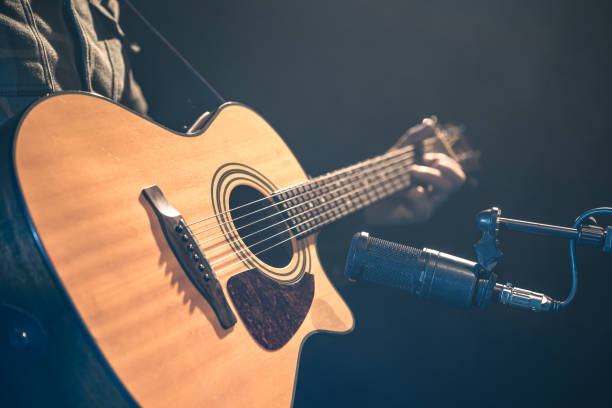 istock Male musician playing acoustic guitar behind microphone in recording studio. 2083882929