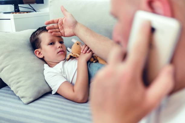 istock Sick little boy in bed while his father uses a hand to check his temperature. Caucasian single parent feeling son's forehead. Cute child feeling ill while his father checks fever. 2083883984