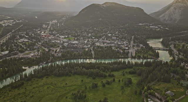 Banff AB Canada Aerial v14 drone flyover stables capturing Bow river, picturesque townscape, forested valley and sun peeking through behind the mountain ranges - Shot with Mavic 3 Pro Cine - July 2023