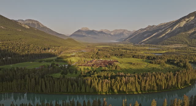 Banff AB Canada Aerial v23 flyover town center and Bow river capturing residential houses, horse stables and sunlight on forested valley and mountain ranges - Shot with Mavic 3 Pro Cine - July 2023