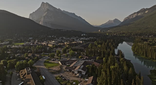 Banff AB Canada Aerial v33 cinematic flyover capturing scenic landscape of train crossing quaint town by the Bow river and Rundle mountain ranges at sunrise - Shot with Mavic 3 Pro Cine - July 2023