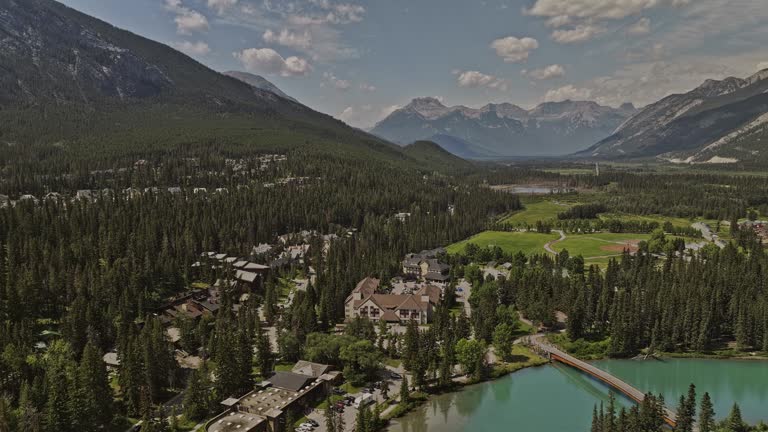 Banff AB Canada Aerial v35 drone flyover town center across glacier-fed Bow river capturing picturesque townscape and landscape of mountain ranges in summer - Shot with Mavic 3 Pro Cine - July 2023