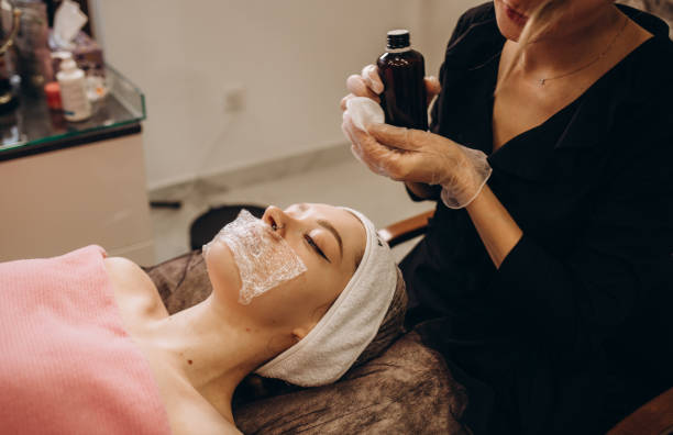 istock Cosmetologist applying mask on client's face in spa salon. 2083963694