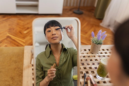 Asian Woman Putting Mascara While Looking in the Mirror in the Living Room