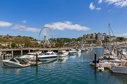 View cross the harbour in the centre of Torquay, UK.  Boats can be seen moored in the harbour.  People can be seen on the promenade