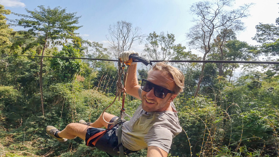 A young man zips through the lush jungle of Laos, immersed in the exhilarating thrill of adventure amidst breathtaking natural scenery.