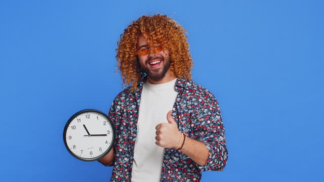Excited Caucasian man showing time hour on wall office clock ok thumb up approve hurry up deadline