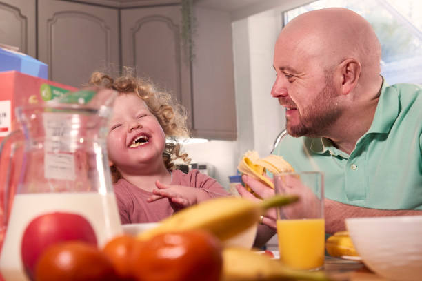 A Dad sat at the kitchen table with his young daughter during breakfast time.