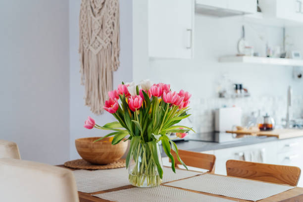 istock Stylish and modern boho, scandi interior of open space white kitchen with pink tulip flowers in vase on the wooden kitchen counter table, macrame on the wall. Cozy Design home decor. Selective focus. 2084062604