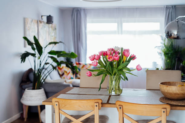 istock Kitchen counter table with focus on vase with huge multicolor tulips bouquet with blurred background of modern cozy living room with couch and green plants. Open space home interior design. 2084063131