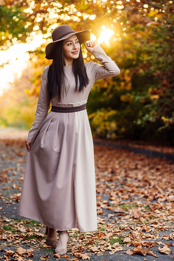Elegantly dressed individual with a wide-brimmed hat enjoying a peaceful walk on a leaf-covered path in october