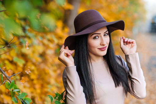 Fashion meets nature. Closeup of cute young woman adjusting wide-brimmed hat amidst autumn splendor.