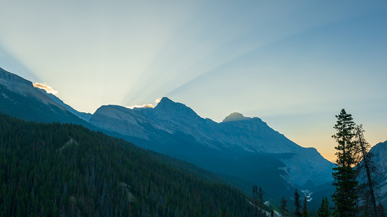 Morning sunrise views along the Icefields Parkway between Banff & Jasper in the Canadian Rockies with stunning sun rays shining bright above the landscape, mountain peaks.