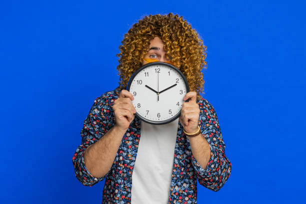 istock Serious strict stylish man holding office clock hiding behind checking time on watch obscuring face 2084101035