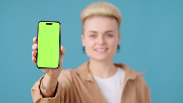 Smiling woman shows smartphone screen with green Chromakey