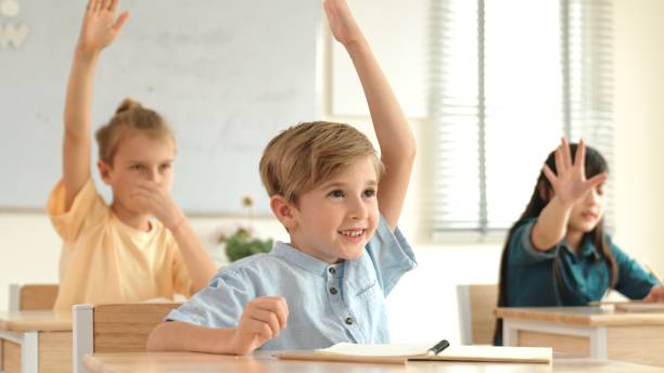 istock Smart caucasian boy raising hand for asking teacher at classroom. Pedagogy. 2084116677