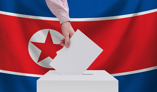 Elections in North Korea. Election concept. A hand throws a ballot into the ballot box. The flag of North Korea on the background.