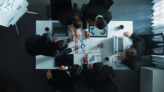 Top down aerial view of business people discussing about financial strategy on table with document and tablet display investment statistic at meeting. Diverse team brainstorm about plan. Directorate.