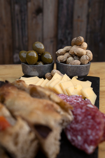 Antipasto. Selective focus on green olives and peanuts, in a cold cuts dish with cheese, salami and focaccia bread.