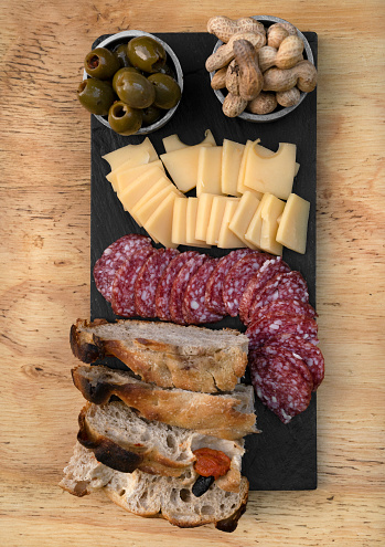 Picada. Top view of a dish with sliced salami, cheese, focaccia peanuts and green olives on the wooden table.
