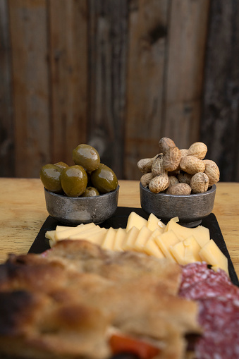 Antipasto. Closeup view of green olives and peanuts, in a cold cuts dish with cheese, salami and focaccia bread.