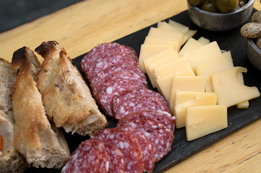 Picada. Top view of a dish with sliced salami, cheese, focaccia peanuts and green olives on the wooden table.