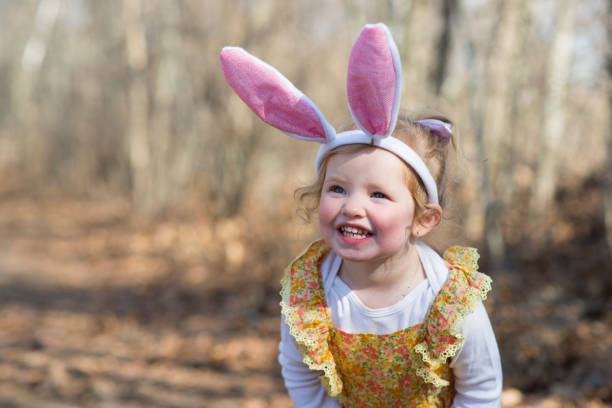 Cute little girl in a yellow flower dress is smiling as she is wearing costume rabbit ears to celebrate Easter and the Easter bunny on a spring morning.