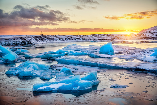 Icebergs floatin and melting at Jokulsarlon glacier lagoon with mountain peaks lit by the warm sunset light, in Iceland. Climate change concept