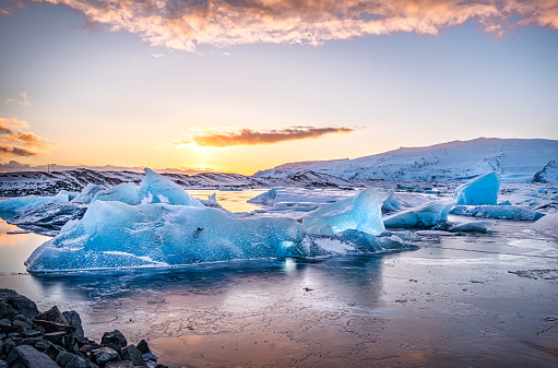 Icebergs floatin at Jokulsarlon glacier lagoon with mountain peaks lit by the warm sunset light, in Iceland.