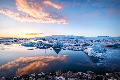 Icebergs floatin at Jokulsarlon glacier lagoon with mountain peaks lit by the warm sunset light, in Iceland.