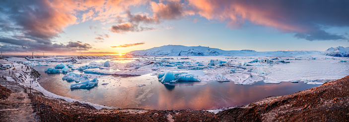 Panoramic view of Icebergs floatin at Jokulsarlon glacier lagoon with mountain peaks lit by the warm sunset light, in Iceland.