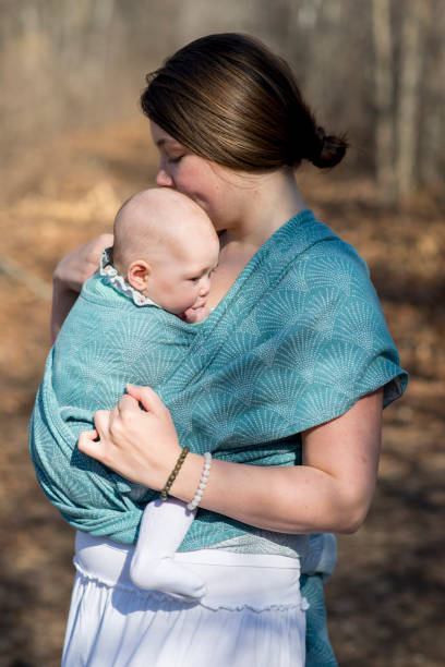 Beautiful young mother is adjusting her sling baby carrier wrap as she is on a walk outdoors in the spring with her beautiful baby girl in the morning.