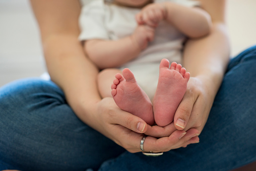 Closeup of cute little baby feet being held by a young mothers hands as she is sitting cross-legged.