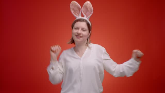 Funny young woman with bunny ears dancing on a red background.