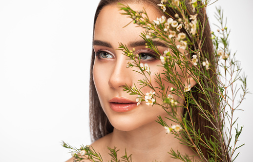 A young beautiful girl with clean skin with beautiful makeup, small pink flowers near her face. Eyebrow lamination. Professional make-up and face care.