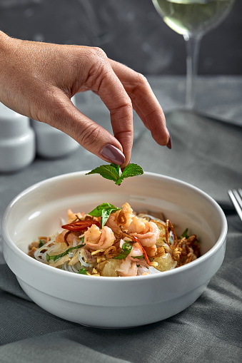 Rice noodles with shrimps and seafood with female hand, spicy asian style noodles in bowl