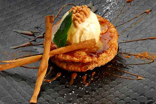 Buñuelos, Fritters covered in honey and cajeta with a scoop of guava ice cream, garnish with cinnamon sticks on a black plate, close up view