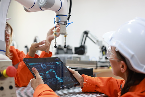 Female maintenance engineer working with the digital tablet  with the robotic arm and analyst chart data static information of examining in laboratory