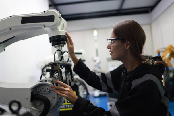 A female mechatronics engineer is working with a robotic arm prototype to examine new programming in the quality room at a manufacturing  welding  factory