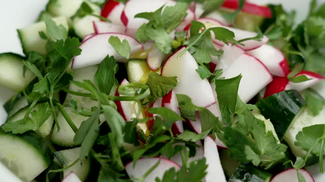 Pouring olive oil into a fresh Mediterranean salad with cucumber, radish and cilantro. Rotation