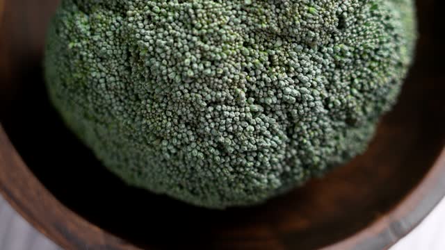 Fresh whole broccoli head in rustic wooden bowl. Raw green vegetable ingredients closeup. Organic healthy food. Rotation. Top view