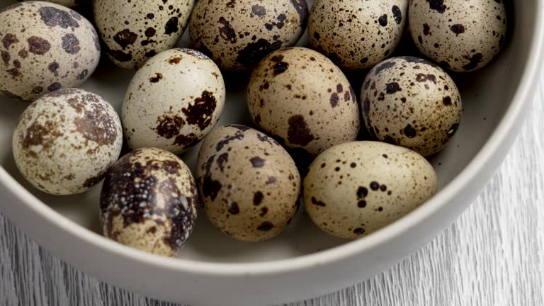 Group of raw fresh quail eggs in a ceramic bowl on a rustic board. Healthy Easter eating. Rotation