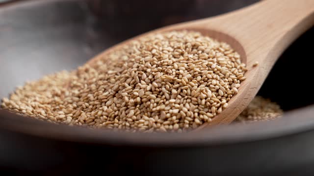 Sesame seasoning seeds in brown bowl with wooden spoon. Culinary ingredients close up. Rotation