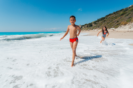 Family enjoys running on the beach and splashing with the waves from the sea on their summer vaction