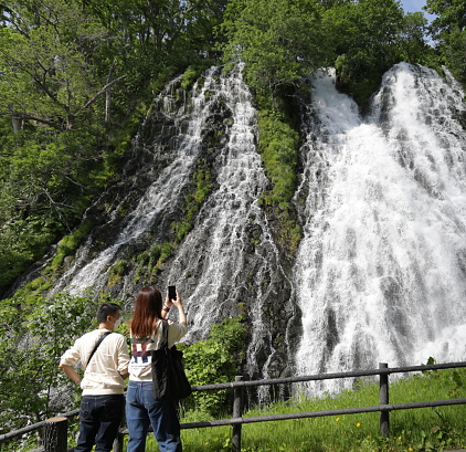 Shari District, Japan - June 1, 2023: Two visitors on an observation deck admire the Waterfall of Oshinkoshin in Utoronishi. Spring afternoon near the Sea of Okhotsk.