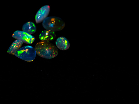 Set of multicolored opals on a black isolated background, oval and rectangular opals of blue, green, pink, Ethiopia.